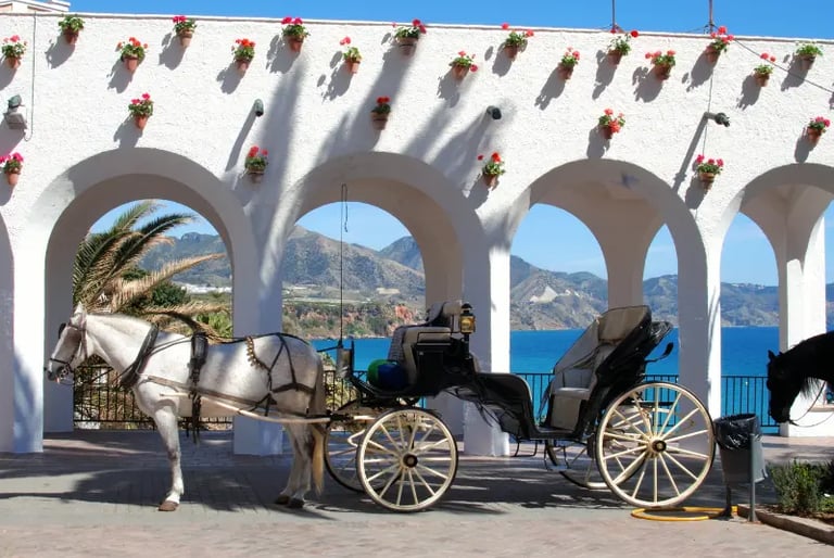 A horse-drawn carriage in Nerja, Spain, parked before white arches overlooking the Mediterranean Sea.