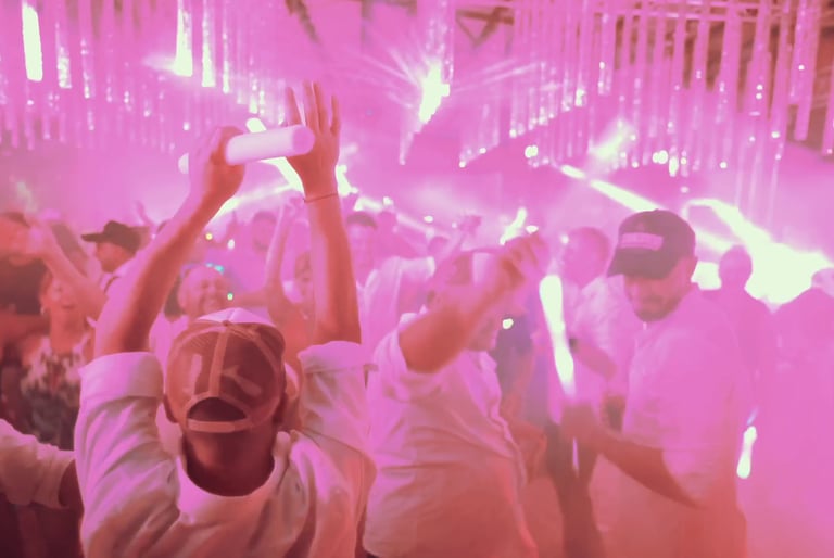 Invitados disfrutando en una pista de baile con iluminación rosada y varas LED en un evento social