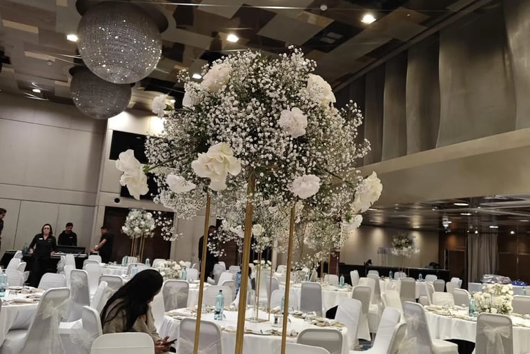 Elegant banquet hall set for an event with white table settings and a large baby's breath floral centerpiece on a gold stand