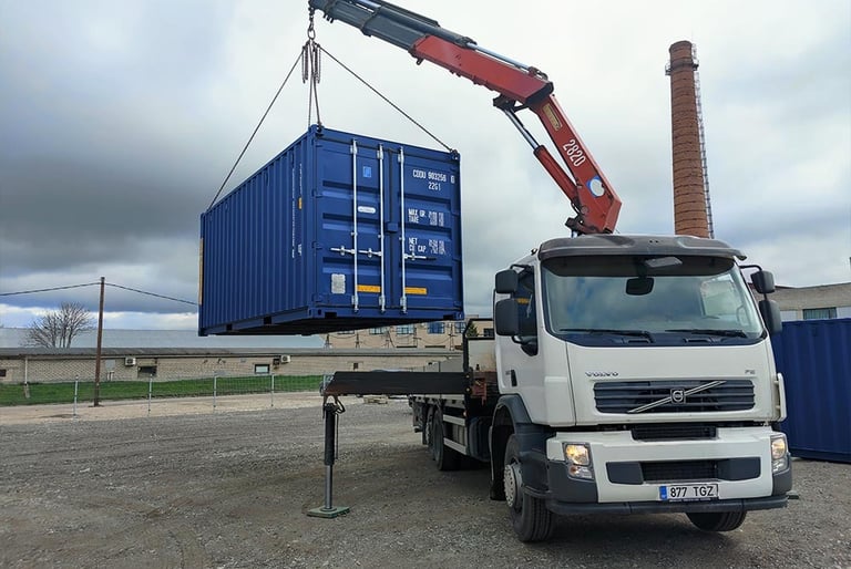 A Volvo crane truck lifting a blue shipping container at an industrial logistics site.