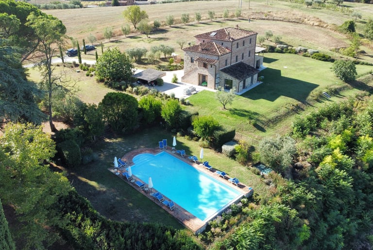 Aerial view of a luxury stone villa in Tuscany with a private swimming pool and lush garden.
