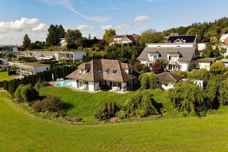 Drohnenaufnahme eines Einfamilienhauses mit Garten, Pool und umliegender Wohngegend