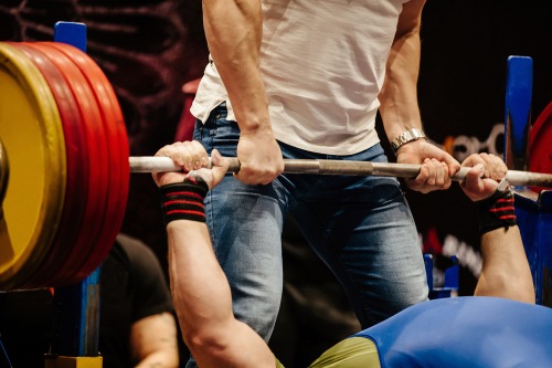 A spotter assists a powerlifter during a heavy bench press with a weighted barbell.