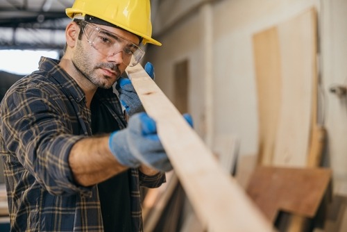 a man in a hard hat and safety glasses is holding a piece of wood