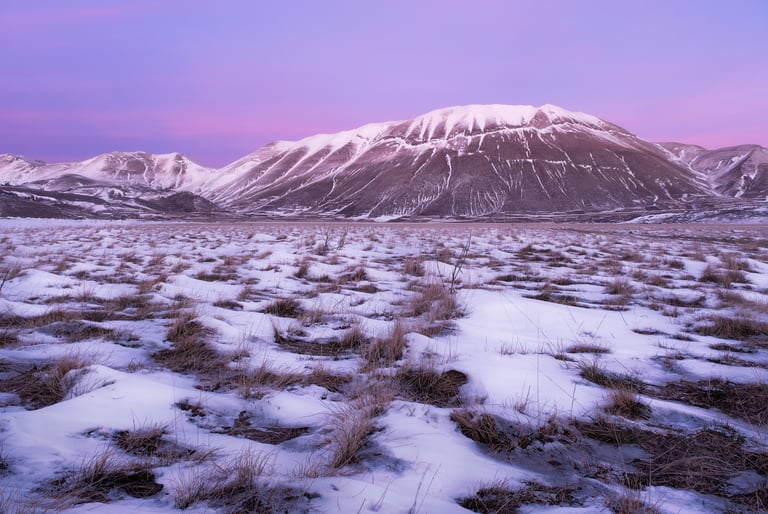 Piana di Castelluccio innevata con tramonto roseo e monti sullo sfondo