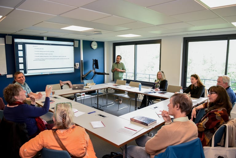 Un groupe d'adulte sont réunis autour d'une table carrée. Ils suivent la conférence d'un intervenant