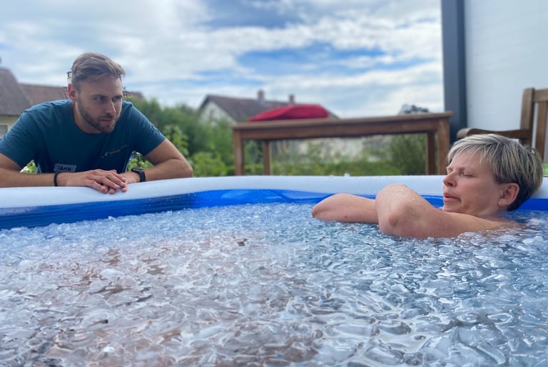 Eine Frau sitzt in tiefer Meditation im Eisbad und wird von einem erfahrenen Wim Hof Instruktor unterstützt
