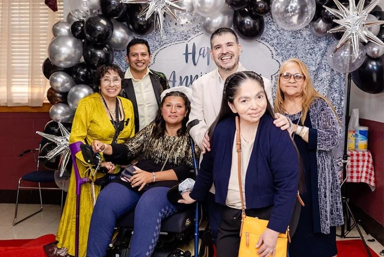 Diverse group of smiling people with disabilities posing at an anniversary party with silver and black balloons.