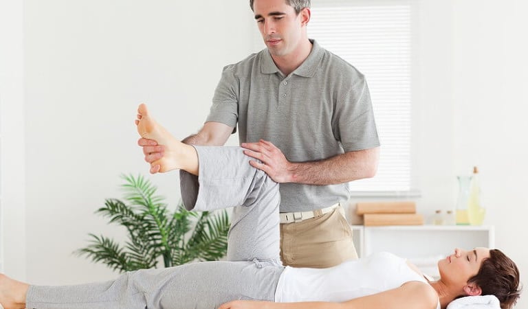 Fisioterapeuta masculino profesional realizando un estiramiento de rodilla y pierna a una paciente e