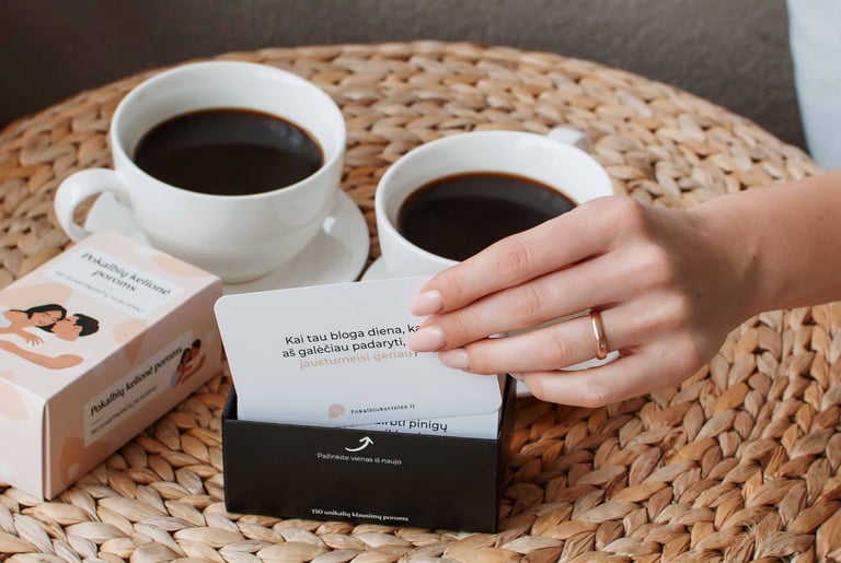 Pokalbių kortelės poroms padėtos šalia kavos puodelių ant pinto stalo padėkliuko.