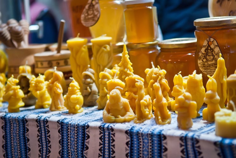 Handmade beeswax candles in various shapes displayed with honey jars at a local market.