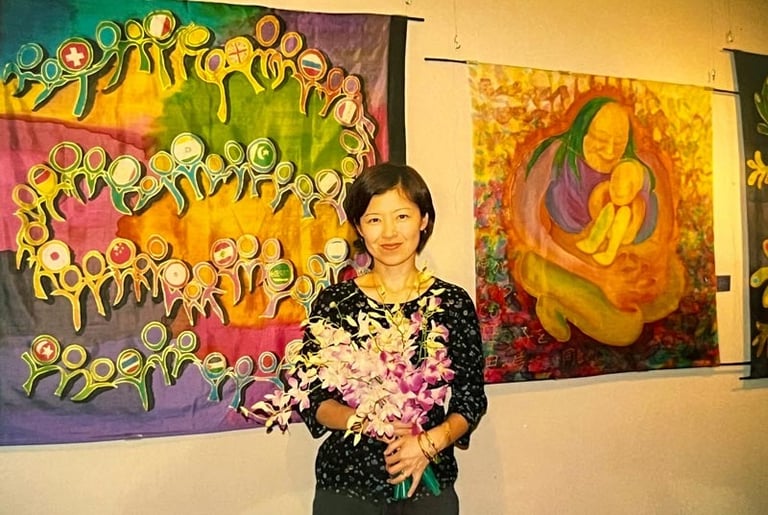 Kayoko standing with a bunch of flowers with two of her textile exhibits in the background.