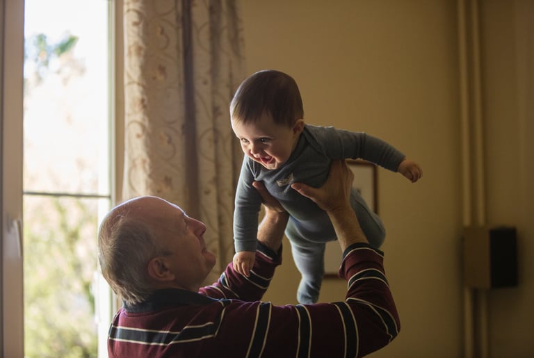 Abuelo levantando a su nieto con una sonrisa, simbolizando la importancia de la estimulación cogniti