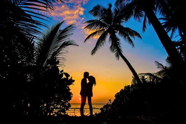 a couple kissing in front of a sunset on a tropical island