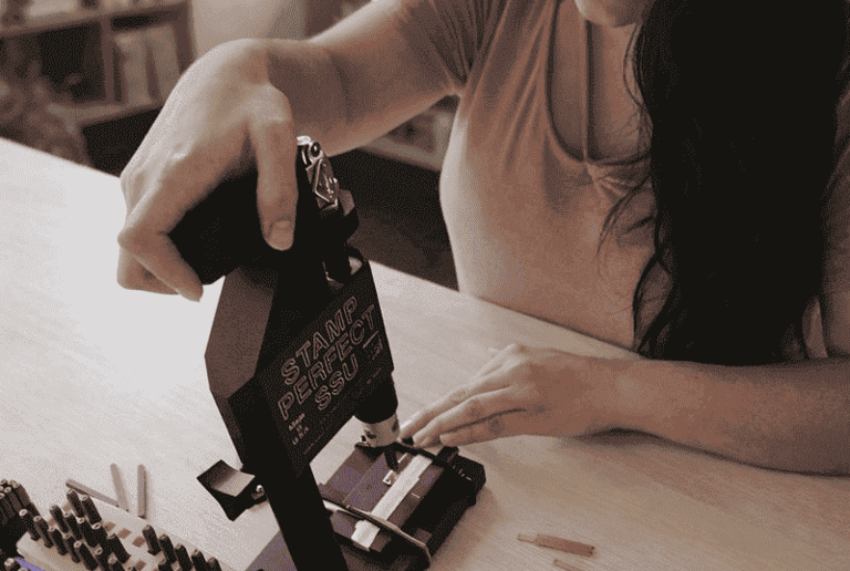 Una mujer utiliza una herramienta de estampado de metal para grabar joyas personalizada