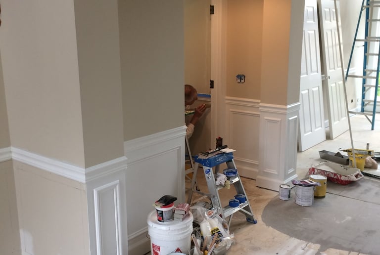 Professional interior home painting project featuring white wainscoting and tan walls with painting supplies.