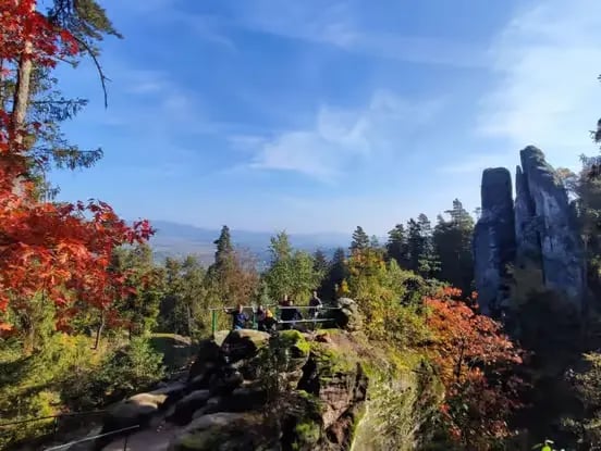 Hikers at a sandstone viewpoint in Bohemian Paradise with fall foliage and rock towers