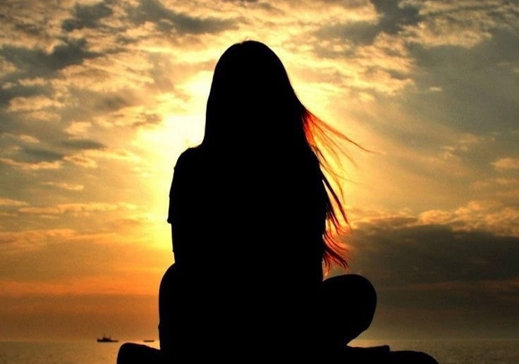 a woman sitting on a bench in front of a sunset