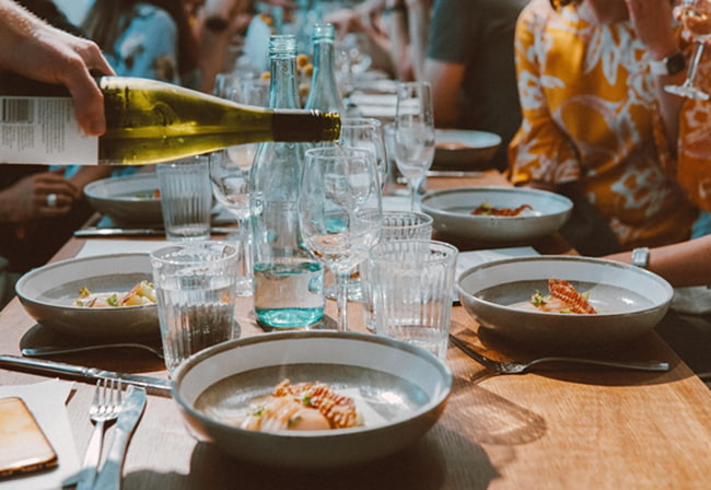 table avec plein de personnes avec un plat réalisé par un partenaire local et dégustation de vin 