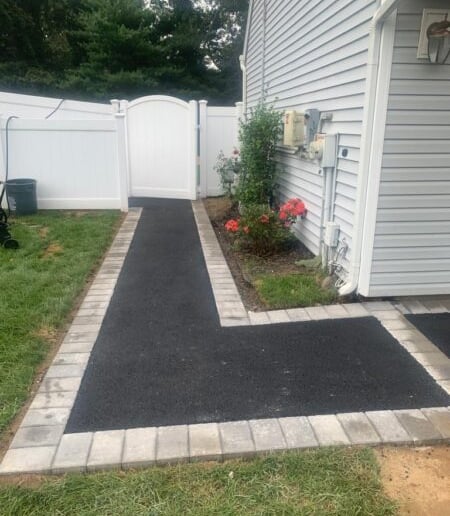 Fresh asphalt walkway with decorative stone paver borders.