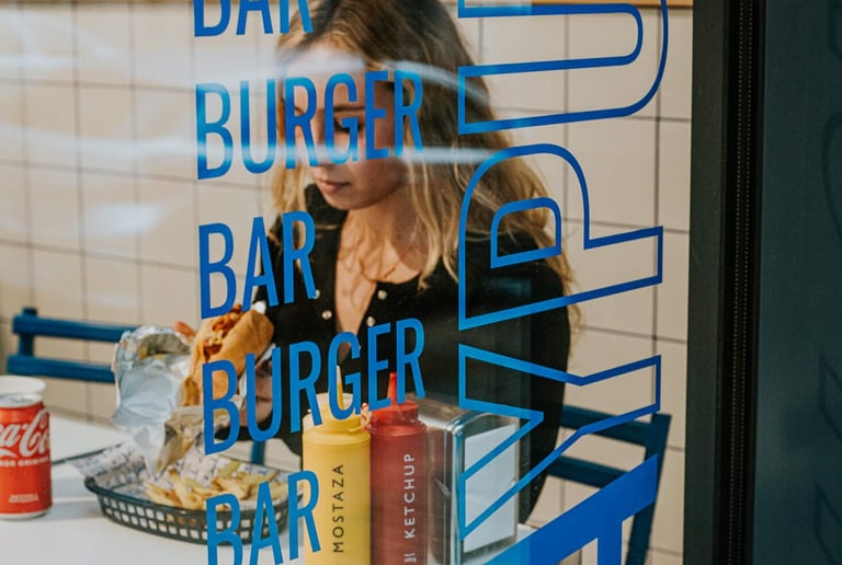 Client gaudint d’una burger a Flipa, vist a través del vidre decorat del local