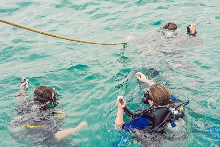 Scuba divers in full gear holding a safety line during a group diving excursion in turquoise ocean water.