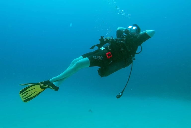 Scuba diver wearing gear relaxing underwater in clear blue ocean water with yellow fins.