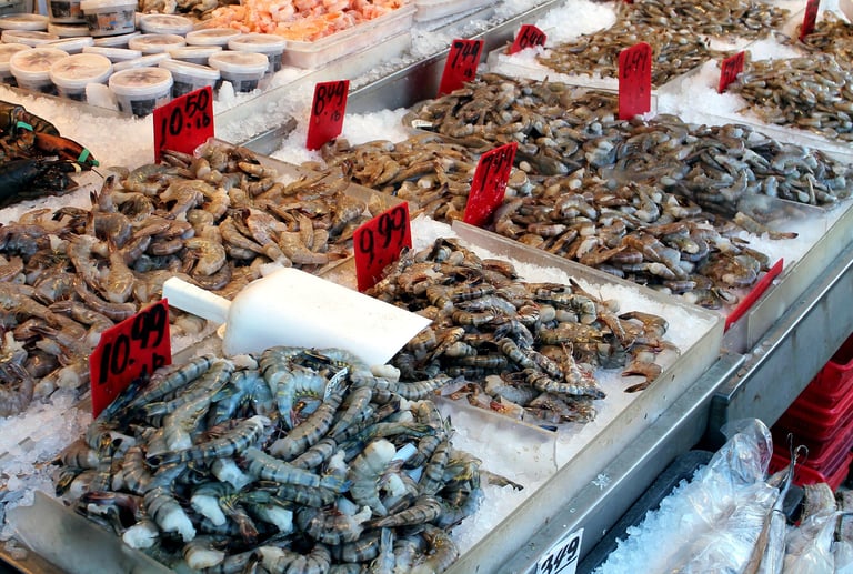 Fresh raw shrimp and prawns on ice at a seafood market display with red price tags.
