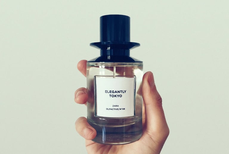 A hand holding a bottle of Zara Elegantly Tokyo Olfactive fragrance against a white background.