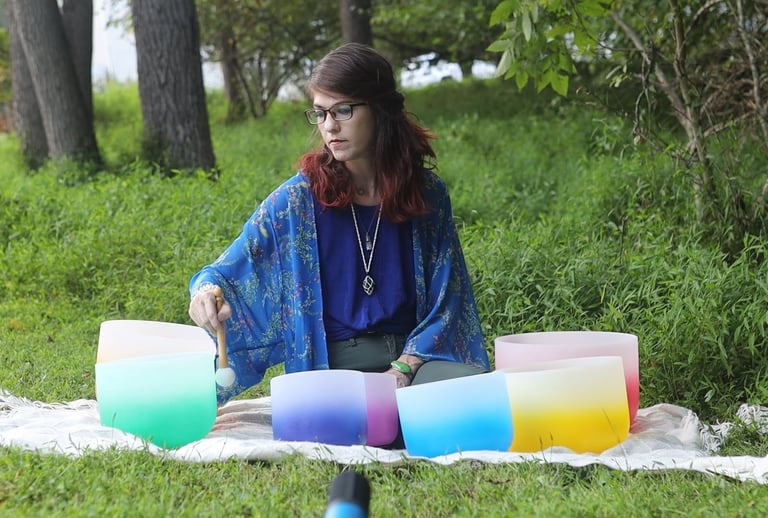 a woman sitting on a blanket playing her crystal singing bowls