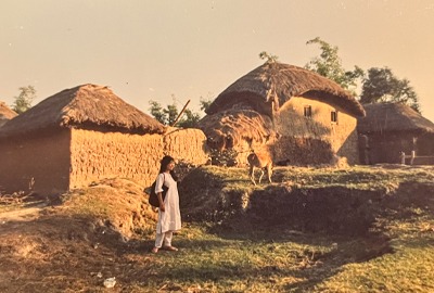 Kayoko standing by large mud and thatch homes.
