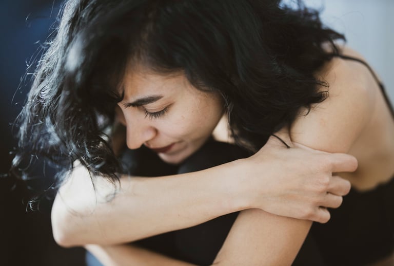 una mujer triste sentada e inclinada hacia delante con sus brazos abrazados