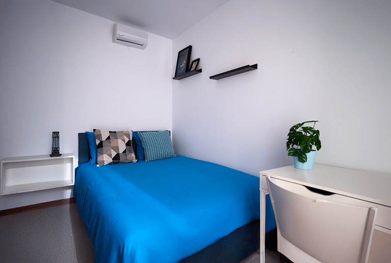 "Una cama azul y un escritorio blanco."