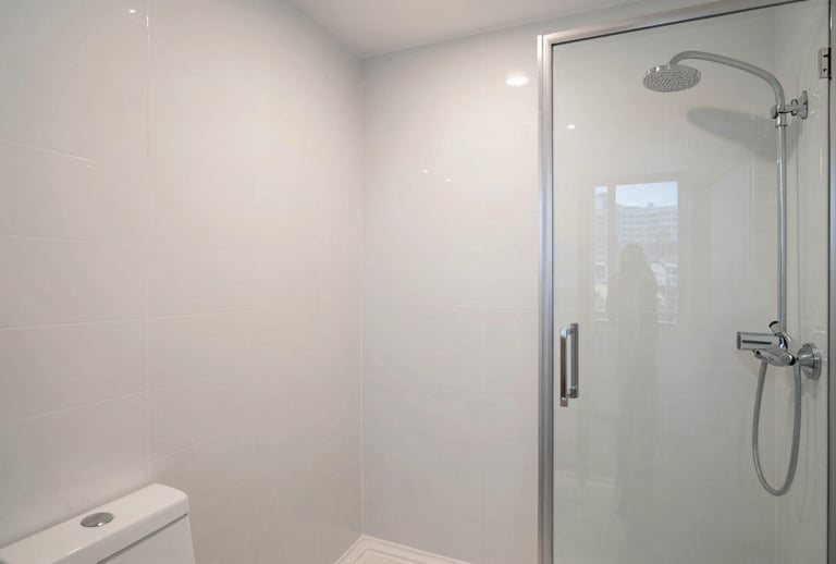 Wide shot of a modern bathroom with newly refinished white wall tiles and a gleaming shower stall in a Manhattan residence. The lighting is crisp and clear, emphasizing a spotless and minimalist look. Professional architectural photography.