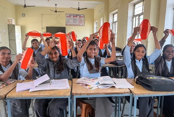 Class of young schoolgirls holding up a Hanaru reusable sanitary napkin in a schoolroom