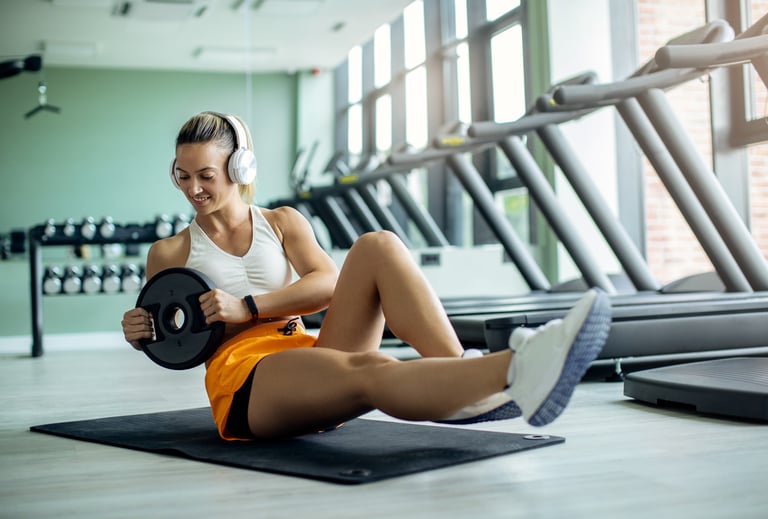 a lady wearing white headphones and doing an abs execise with a weighted plate