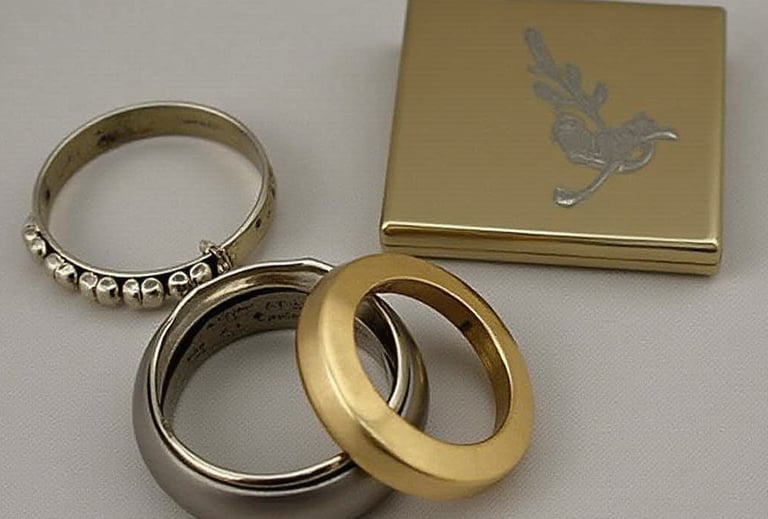 Engraved Elegant gold & silver wedding rings displayed next to a vintage engraved metal jewelry box.