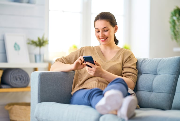 Smiling woman using a smartphone while relaxing on a sofa while waiting for her mobile mechanic.