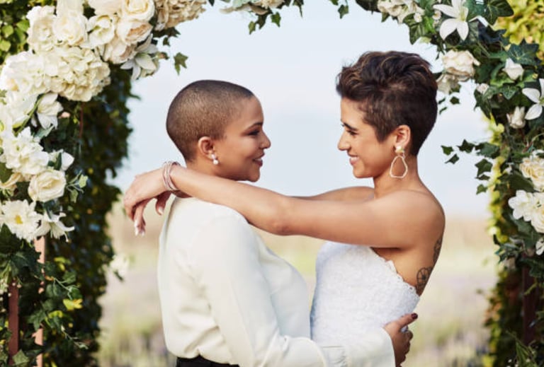 a lesbian couple at their wedding celebration under the arbour / bower dress in white 