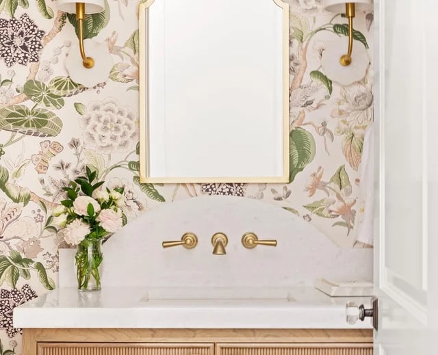 Elegant bathroom vanity with floral wallpaper, gold mirror, and marble countertop.