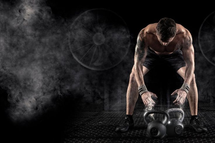 Homem musculoso em academia escura curvado sobre kettlebells com pó de magnésio pronto pro treino