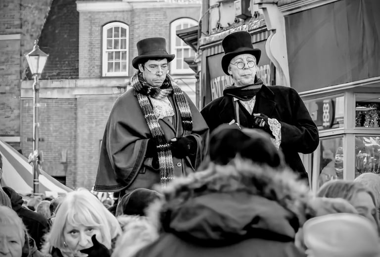 Performers in Victorian costumes with top hats and capes at a Dickensian Christmas festival.