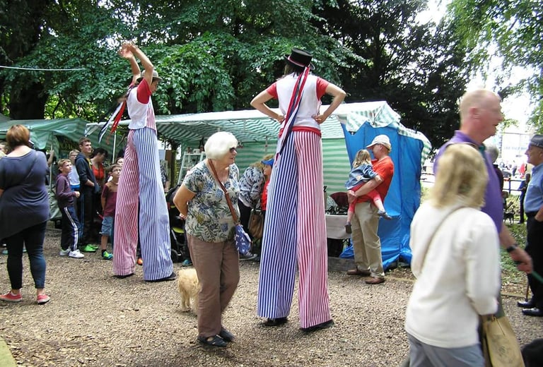 Two street performers on high stilts in red and blue striped costumes entertain a crowd at an outdoor festival.