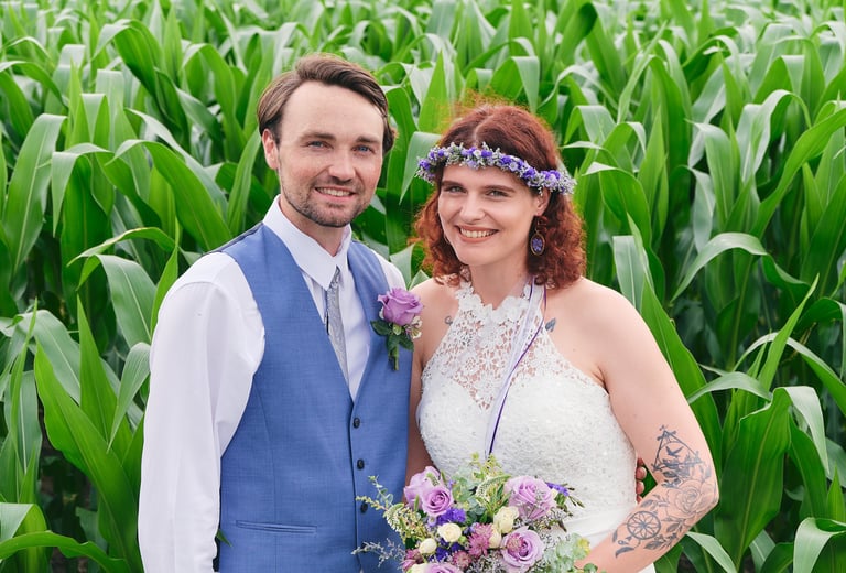 a bride holding a bouquet and a groom standing next to each other in a corn field