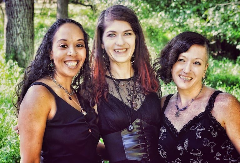 three women in black dresses standing in a forest