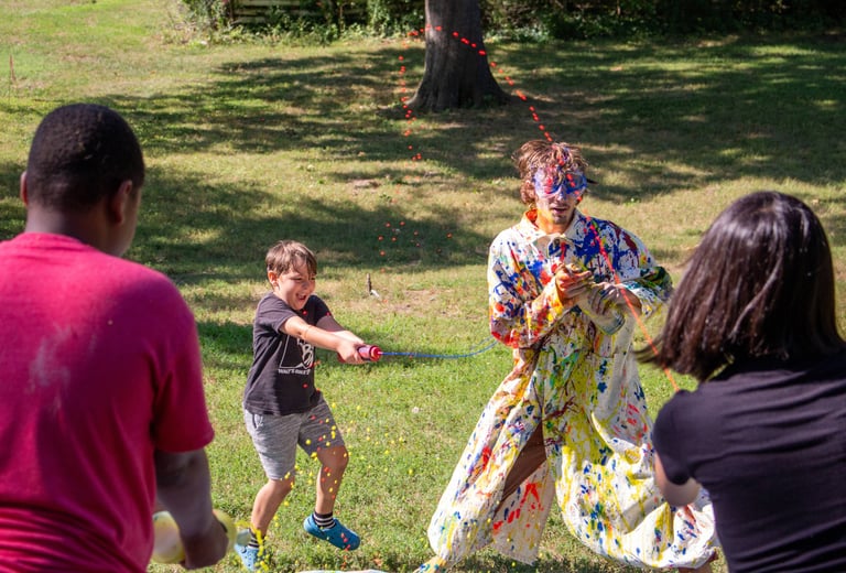 Summer Camp children shooting paint at the teacher in a white trenchcoat.