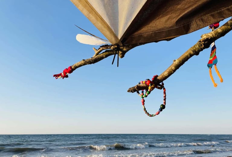 Handmade bead bracelets and colorful ribbons hanging from a tree branch on a sunny beach.