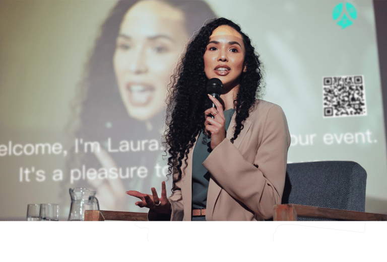 a woman in a suit and a microphone in front of a screen while ohaio livespeaker works