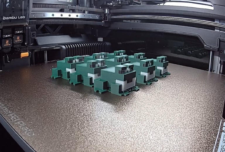 Bambu Lab 3D printer bed with a batch of green blocky toy frogs printed on a textured PEI plate.