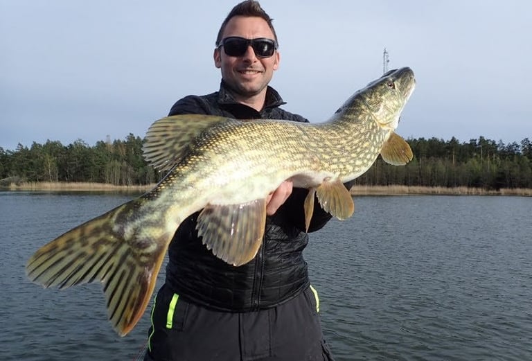 Ein Fischer hält einen Hecht in der Hand.